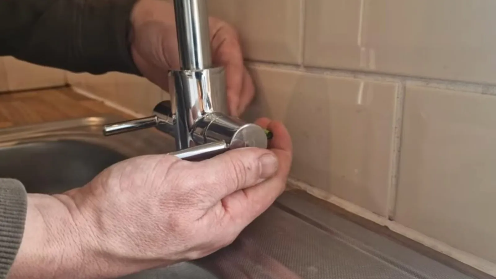 Hands repairing a kitchen faucet at the sink